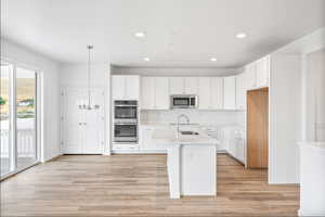 Kitchen featuring white cabinets, stainless steel appliances, a kitchen island with sink, and light wood finished floors