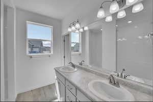 Full bathroom with double vanity, light wood-type flooring, and tiled shower