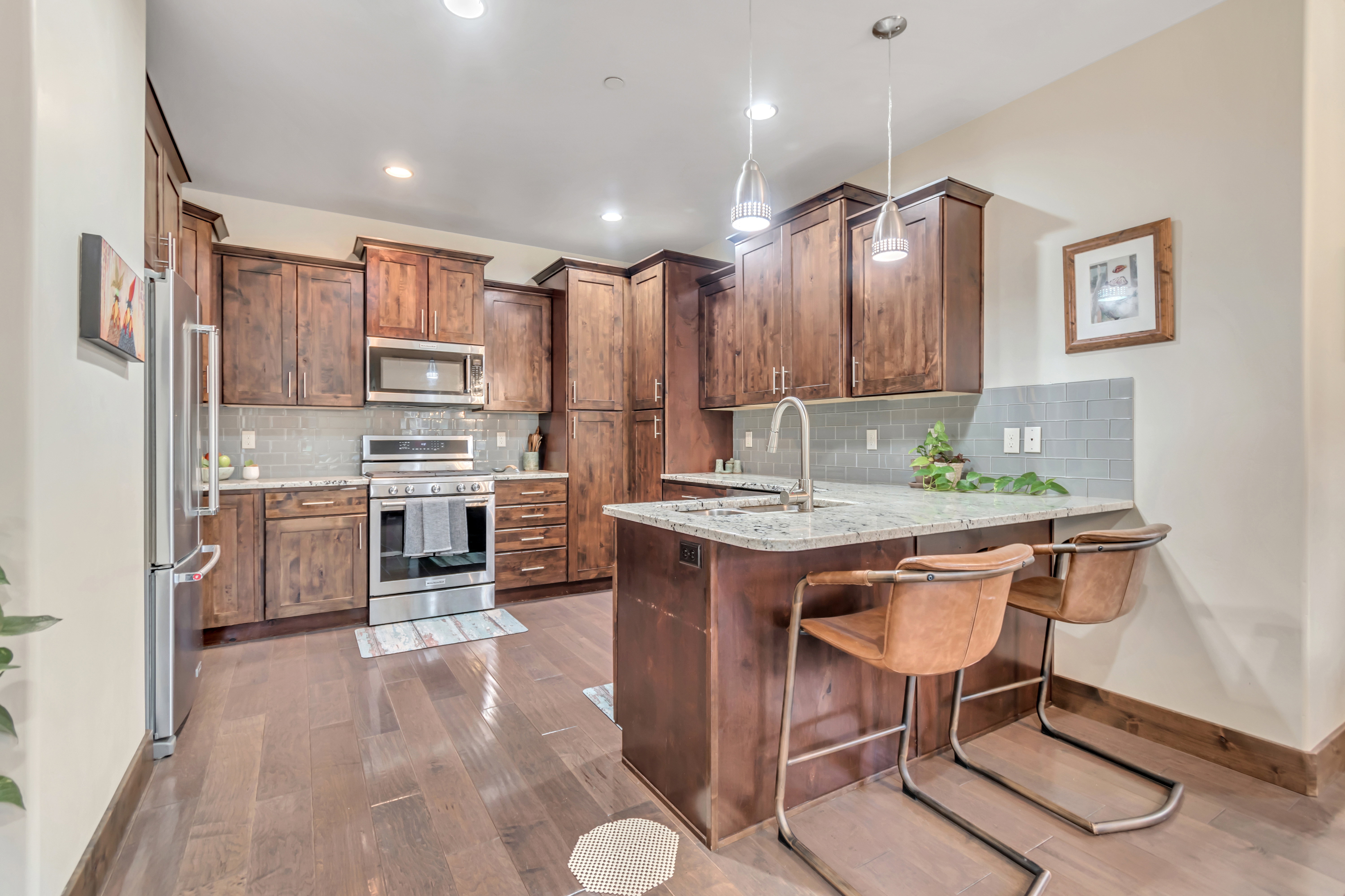 Kitchen with stainless steel appliances, a peninsula, light stone counters, a breakfast bar, and pendant lighting