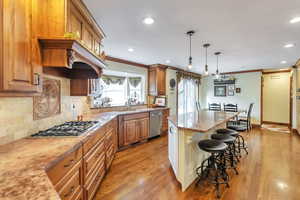 Dual tone kitchen featuring custom cabinets, ornamental molding, a kitchen island, a kitchen breakfast bar, light wood finished floors, and decorative light fixtures