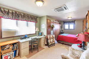 Bedroom with light colored carpet, a desk, and a textured ceiling