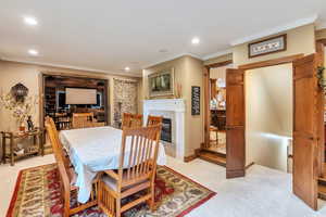 Dining space with light colored carpet, ornamental molding, a glass covered fireplace, and recessed lighting