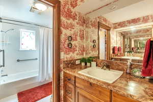 Full bathroom featuring vanity, shower / tub combo, and wallpapered walls