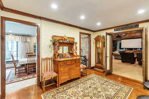 Sitting room with light wood-type flooring, ornamental molding, and recessed lighting