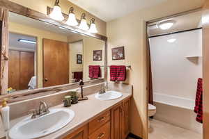 Bathroom featuring double vanity, a textured ceiling, connected bathroom, light tile patterned floors, and shower / bath combination