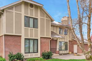 Back of house with brick siding, stucco siding, a chimney, and a patio area
