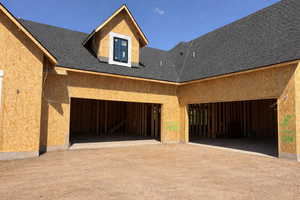 View of property exterior with a garage, roof with shingles, dirt driveway, and stucco siding