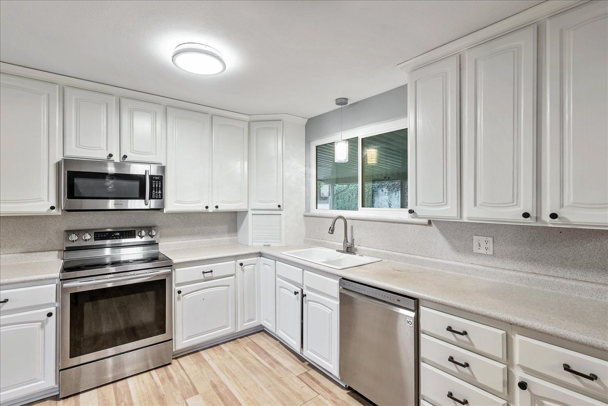 Kitchen featuring stainless steel appliances, white cabinets, light countertops, and light wood-style flooring