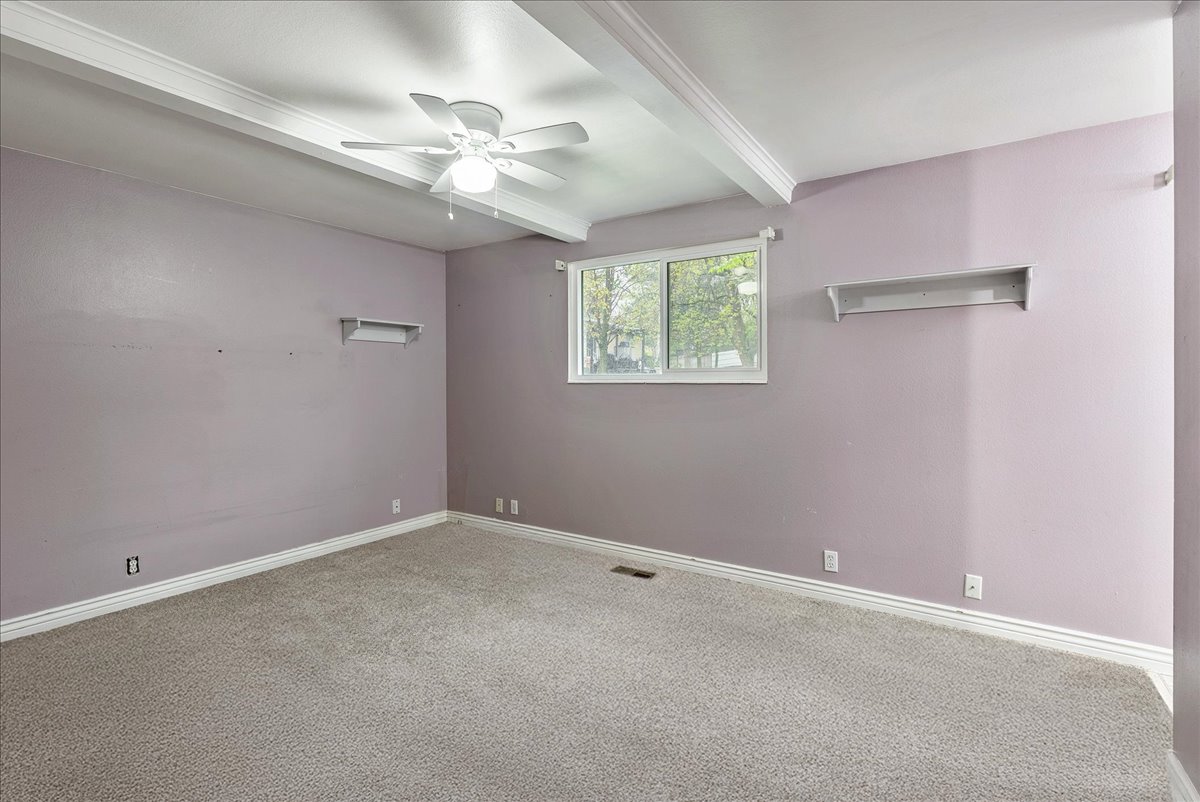 Empty room featuring beamed ceiling, ceiling fan, and carpet flooring