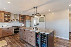 Dual tone kitchen featuring light stone countertops, stainless steel appliances, beverage cooler, pendant lighting, and dual tone cabinets