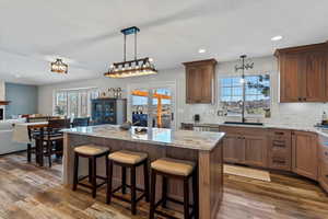 Kitchen with a kitchen bar, light stone counters, pendant lighting, and wood finish cabinets