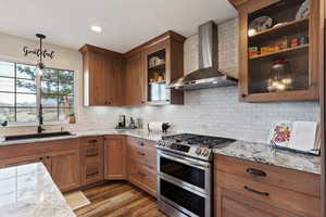 Kitchen with double oven range, pendant lighting, light stone counters, wood finish cabinets, and light wood-style flooring