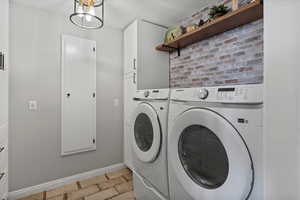 Laundry room with washing machine and clothes dryer, ironing board,  brick wall, stone tile floors, cabinet space, and a textured ceiling