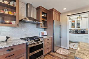 Dual tone kitchen featuring glass fronted cabinets, stainless steel appliances, light stone countertops, light wood-style floors, butler pantry