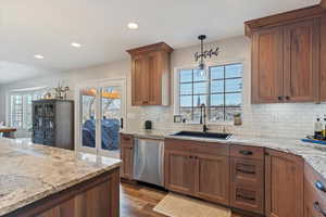 Kitchen featuring wood finish cabinetry, dishwasher, light stone countertops, hanging light fixtures, and dark wood-type flooring