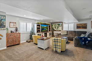 Carpeted living room with a textured ceiling, plantation shutters, and recessed lighting