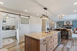 Dual tone kitchen with a kitchen island, light stone counters, open floor plan, , and a barn door, butler pantry