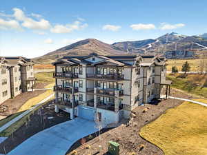 View of front of home with an attached garage, concrete driveway, a mountain view, a balcony, and stone siding