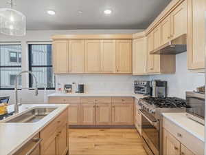 Kitchen with light wood finish cabinets, stainless steel appliances, light wood finished floors, light stone counters, and hanging light fixtures