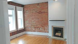 Unfurnished living room featuring brick wall, light wood finished floors, and a fireplace with flush hearth