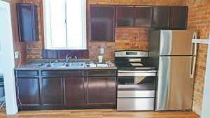 Kitchen with stainless steel appliances, dark wood finish cabinets, brick wall, and light wood-style floors