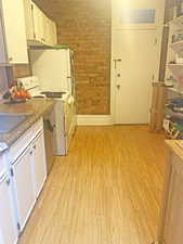 Kitchen featuring white appliances, light wood finished floors, brick wall, white cabinetry, and dark countertops