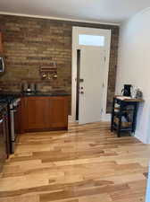 Kitchen featuring brick wall, stainless steel appliances, wood finish cabinets, light wood-type flooring, and ornamental molding