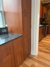 Kitchen with wood finish cabinetry, dark stone counters, light wood finished floors, stainless steel appliances, and tasteful backsplash