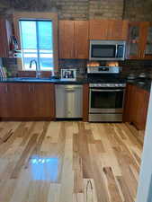 Kitchen featuring stainless steel appliances, wood finish cabinets, light wood-style flooring, glass insert cabinets, and dark stone counters