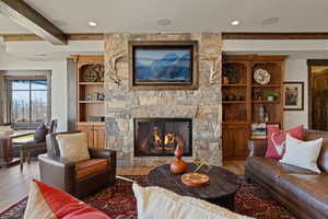 Family room area with a stone fireplace, tv with surround sound, beam ceiling, and wood finished floors
