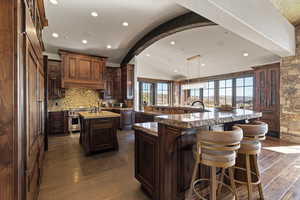 Kitchen with vaulted ceiling, dark wood-style floors, a breakfast bar, luxury stove, and hanging light fixtures