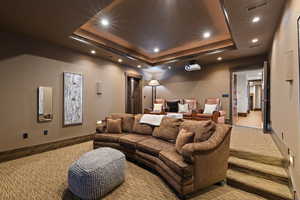 Home theater featuring stadium seating, a tray ceiling and recessed lighting