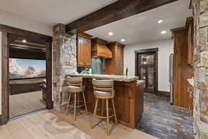Kitchenette/Bar with wood finish cabinetry, beamed ceiling, dark wood-style floors, a kitchen bar, and a peninsula
