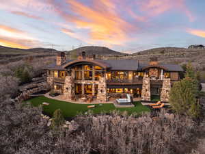 Back of property at dusk with a balcony, a chimney, stone siding, and a patio area