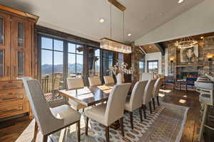 Dining area featuring vaulted ceiling, a mountain view, dark wood-style flooring, a chandelier, and a stone fireplace