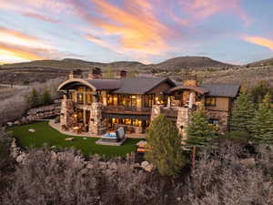 Back of house at dusk with a chimney, a balcony, stone siding, and a mountain view