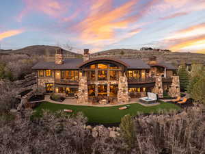 Back of property featuring a balcony, a chimney, a patio, and stone siding