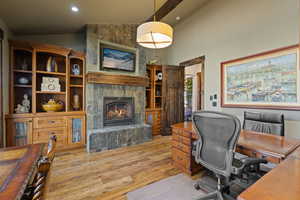 Main level Bedroom/Office featuring built-in cabinets, lofted ceiling, a fireplace, recessed lighting, and light wood finished floors