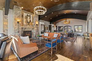 Living area featuring a chandelier, hardwood / wood-style flooring, a stone fireplace, arched walkways, and a barrel ceiling