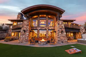 Back of property featuring a balcony, stone siding, an outdoor fire pit, a lawn, and a patio
