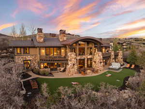 Back of property with stone siding, a patio, a lawn, a balcony, and a chimney