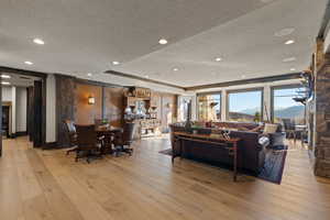 Family game room with a textured ceiling, light wood finished floors, a raised ceiling, a mountain view, and recessed lighting