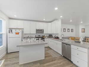 Kitchen with stainless steel appliances, white cabinetry, light wood-type flooring, a breakfast bar area, and a center island