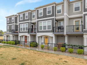 View of front facade with a fenced front yard, stucco siding, board and batten siding, and a balcony