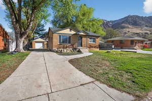 Bungalow with a garage, an outdoor structure, brick siding, a front yard, and a mountain view