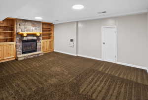 Unfurnished living room with dark colored carpet, built in shelves, and a stone fireplace