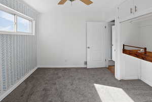Unfurnished bedroom featuring wallpapered walls, an accent wall, carpet floors, and ceiling fan