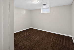 Spare room featuring dark carpet and a textured ceiling