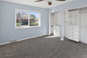 Unfurnished bedroom featuring dark colored carpet, multiple closets, and a ceiling fan