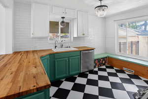Kitchen featuring wood counters, two tone color scheme, stainless steel dishwasher, dark flooring, and backsplash